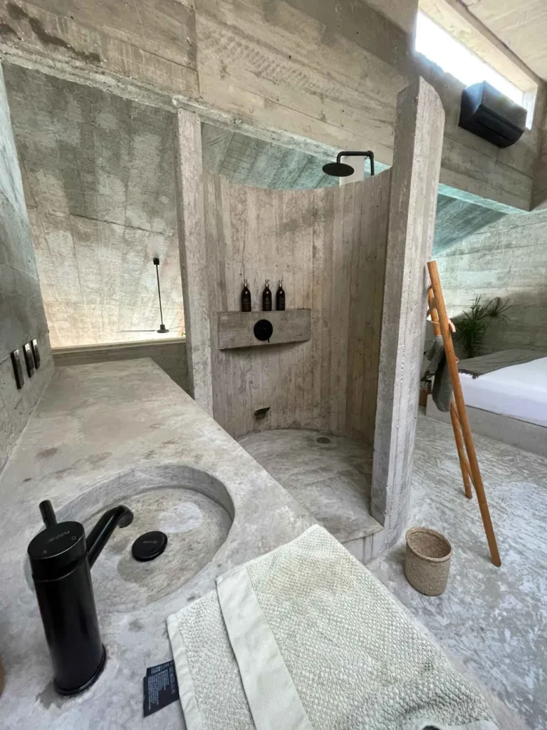 unique architecture at Casa VO in Puerto Escondido modern open bathroom area in grey with a sink, shower and bed in the back and black fittings in the bathroom area at casa vo in puerto escondido