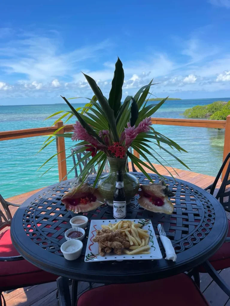 lunch with a view on a round small table with a food plate sauces, a beer and some shell and flower arrangement decoration facing the blue sea