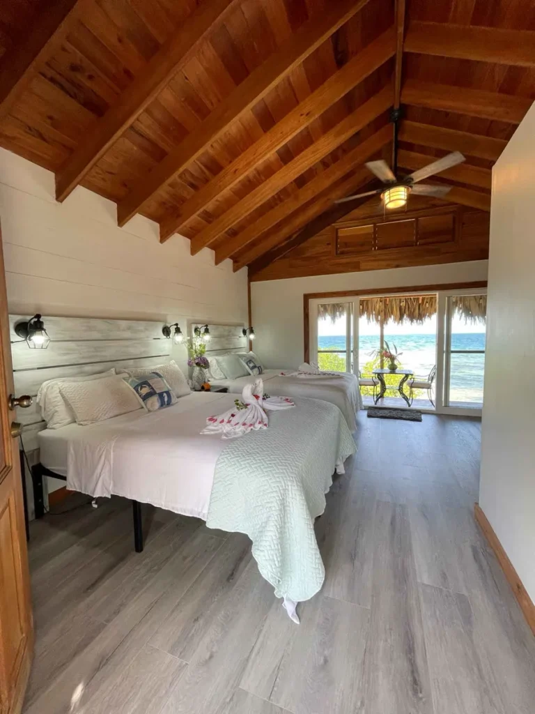 inside the casita with a wooden roof white walls two white double beds and a window front facing the beach and the sea, accommodation for up to 8 persons on your private island little peter oasis in belize