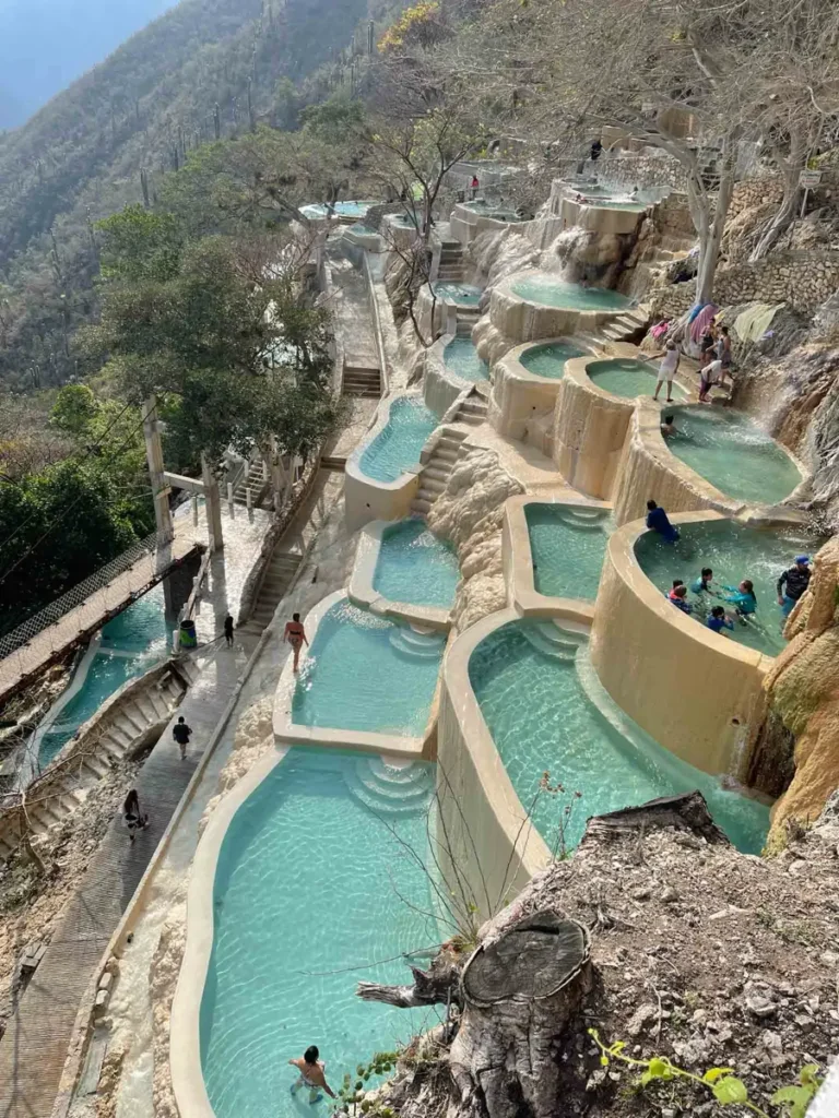 people in multiple blue pools along a dry mountain area, pools are connected via multiple stairs