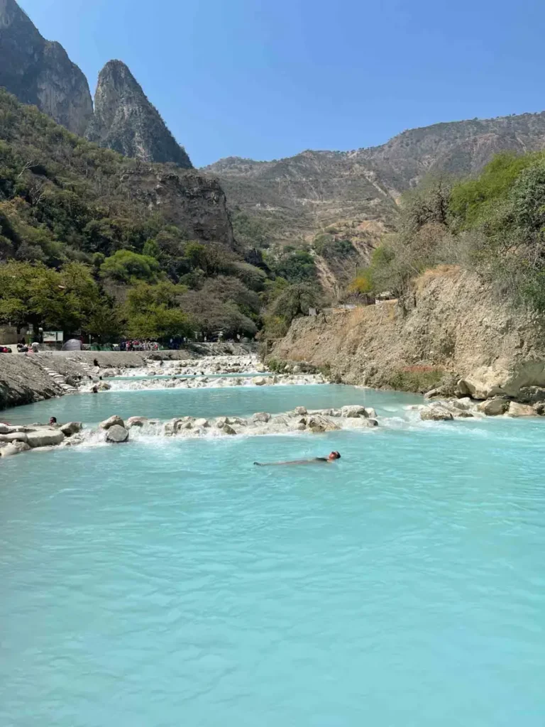 woman floating in a blue wide river surrounded by dry landscape with a few mountains, Grutas de Tolantongo in Hidalgo, Mexico