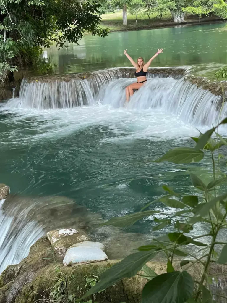 woman laying on a wide multiple layered waterfall stretching her arms in the air surrounded by a forest or jungle nature at Hacienda Gomez Y Sus 7 Cascadas in Mexico