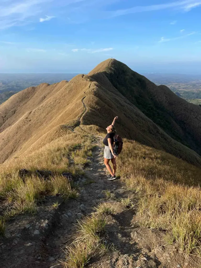 woman standing on a hiking trail with grassy landscapes with shorts, tshirt and a backpack