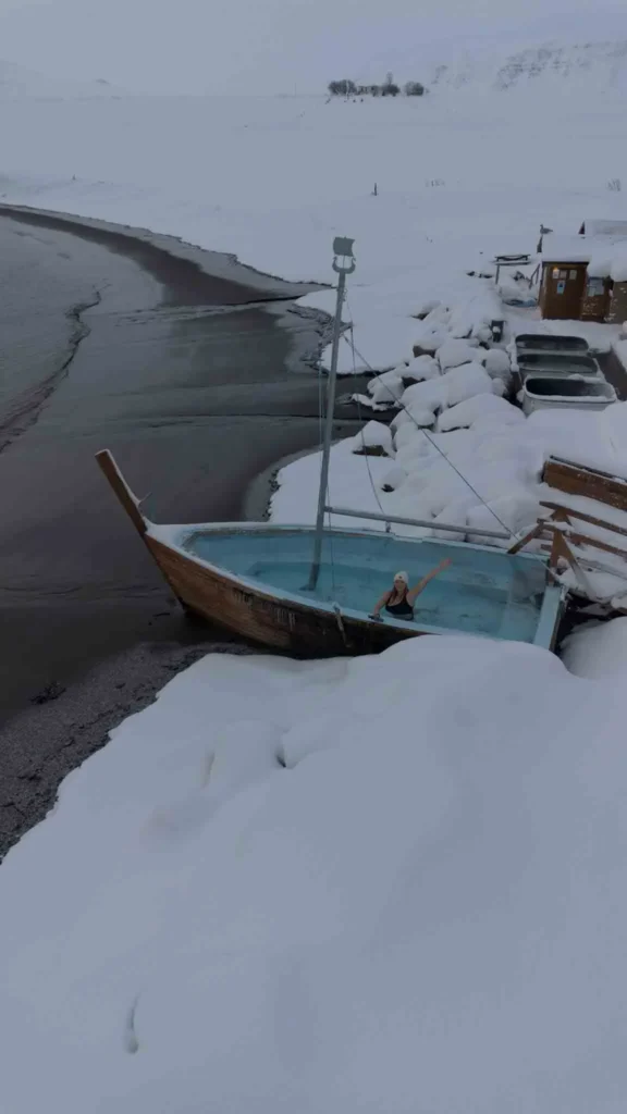 boat hot tub on a beach with three other normal hot tubs on the beach in a snowy landscape at huaganes hot tubs in iceland
