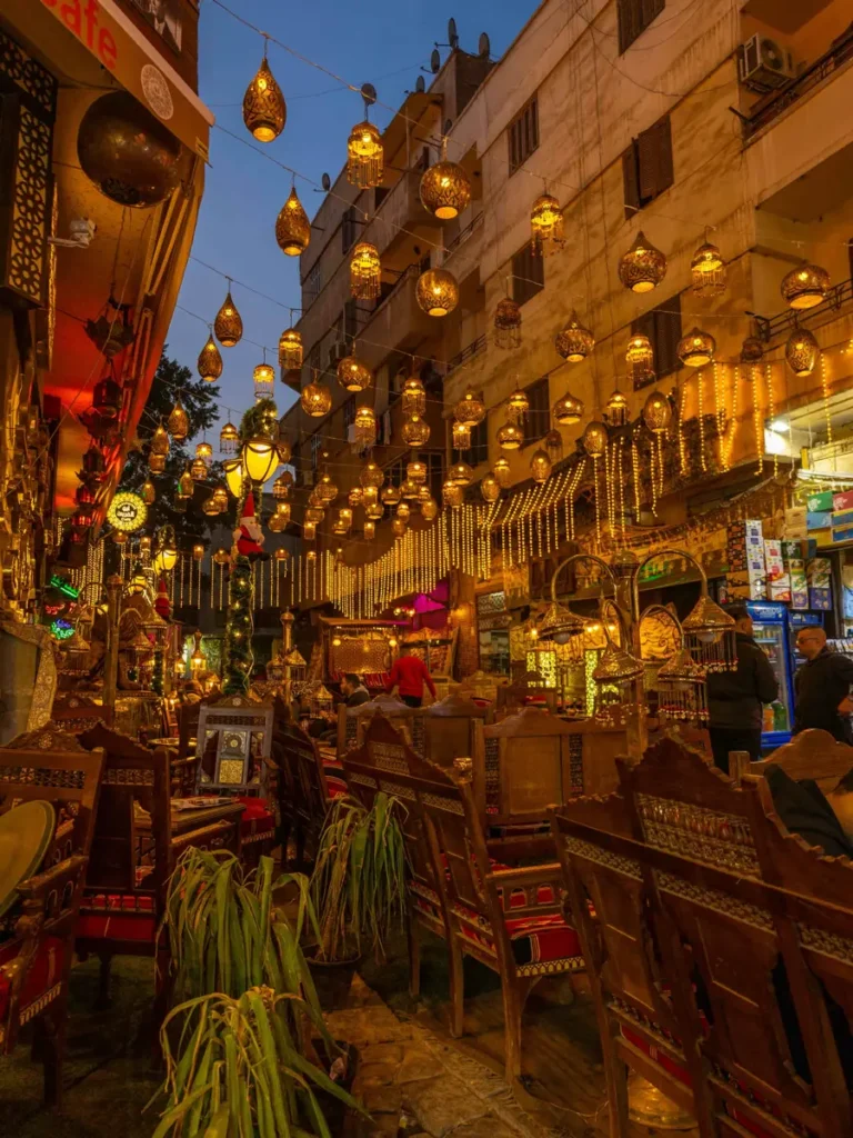 outdoor cafe in an old town with many illuminated lanterns hanging above the cafe between houses