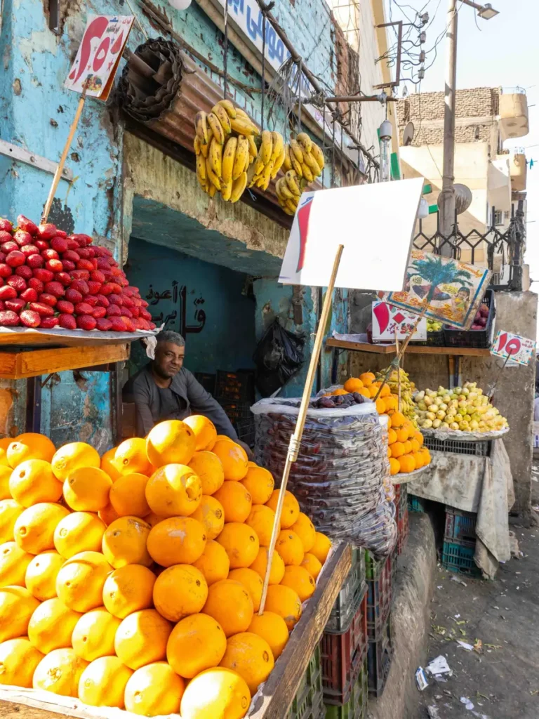 a local vendor selling fresh fruit at a market including oranges and bananas