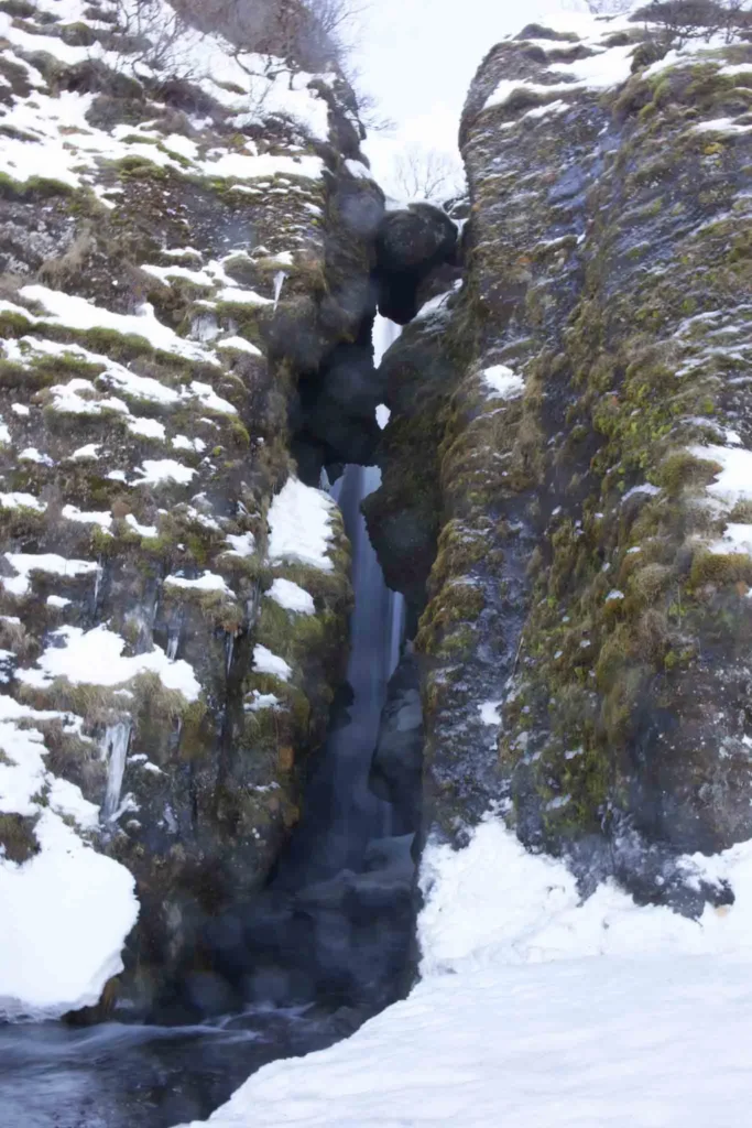 Gljufrabuj – one of the best hidden gems in Iceland split in the black rocky terrain with a waterfall in between with partially snow at hidden gem gljufrabui waterfall in iceland