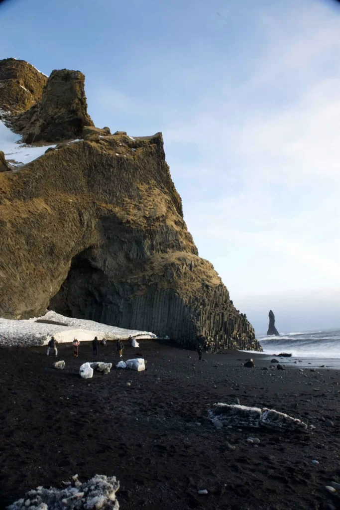 black sand beach Reynisdrangar Beach with some rocks and a big cave with some interesting rock formation, snow and waves in iceland