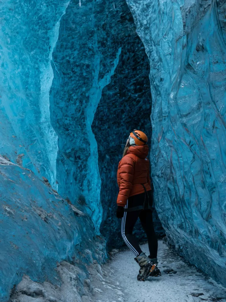 road trip itinerary Iceland woman in an orange winter jacket standing inside the Vatnajökull glacier in iceland