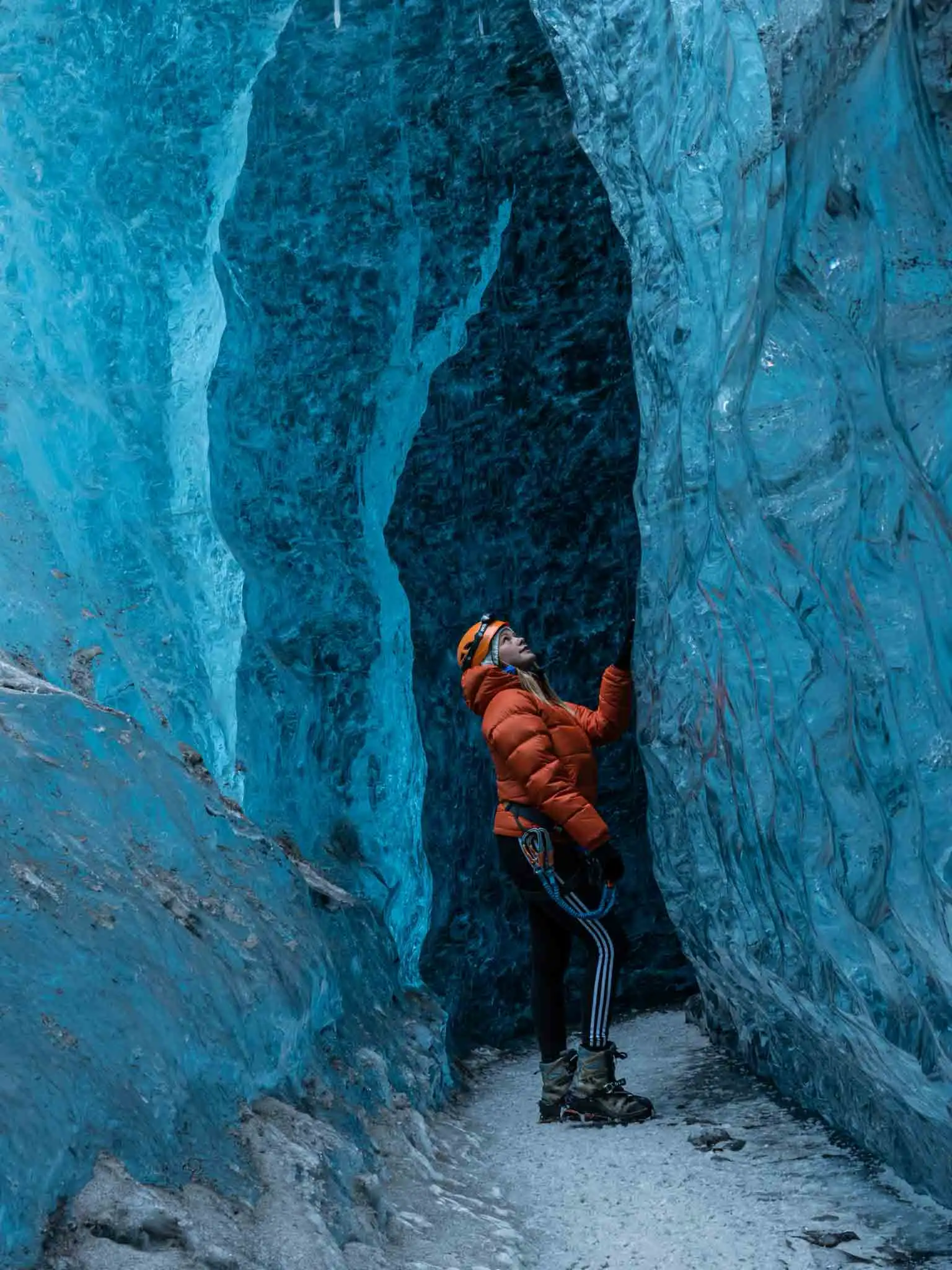 Kvernufoss woman in an orange winter jacket standing inside an blue ice cave