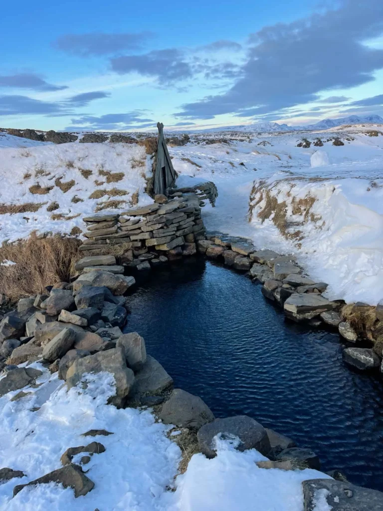 small hut next to hot springs surrounded by stacked stones in a snowy landscape at hrunalaug hot springs in iceland