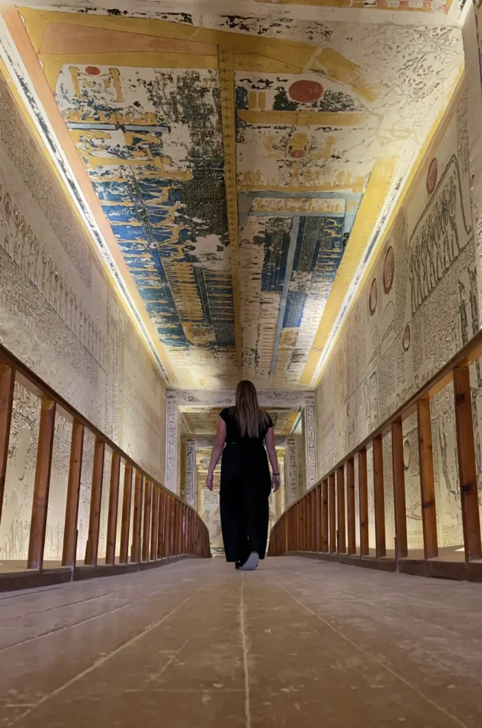 woman walking on the wooden boardwalk of a tomb with colourful paintings and hieropglyhs