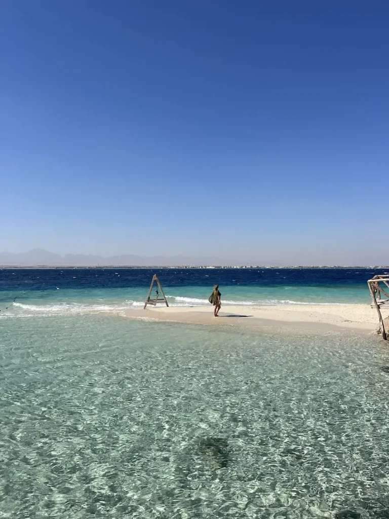 woman standing on a sandbank surrounded by crstal clear blue ocean and blue skies