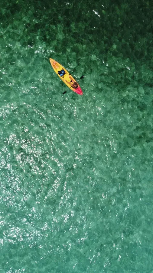drone view of a person in a yellow kayak in clear blue and green water in san pedro belize