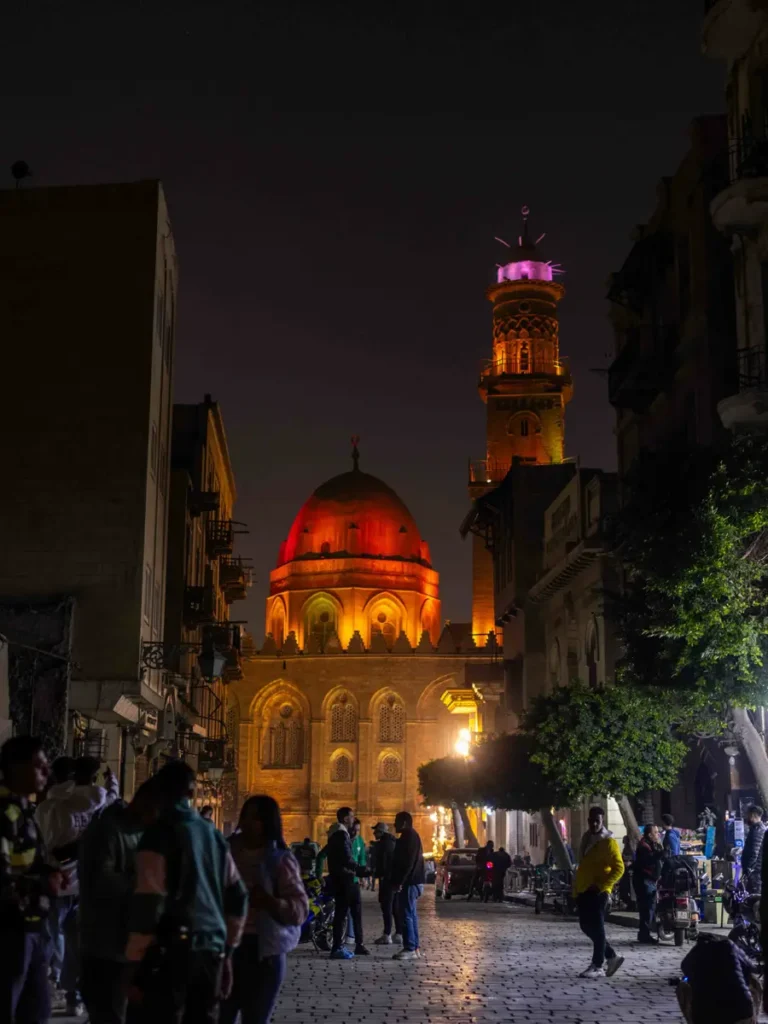 illuminated mosque at night on a street with people strolling around