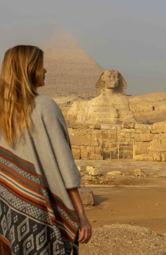 blonde woman looking at a statue and pyramid in the distance
