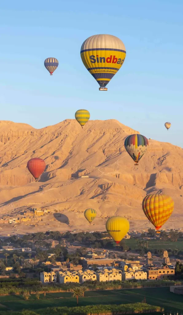 multiple colourful hot air balloons flying over fields and a temple