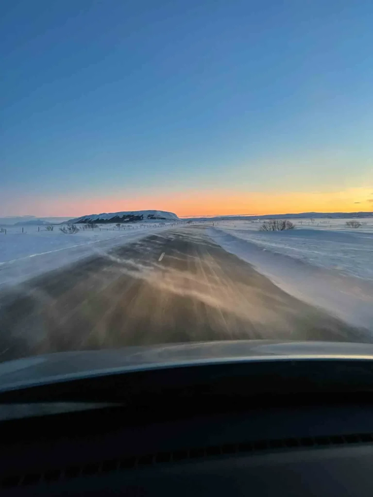 road conditions in Iceland in winter can be tough photo from inside the car with a road and a small snow storm in a snowy lanscape at sunrise or sunset in iceland