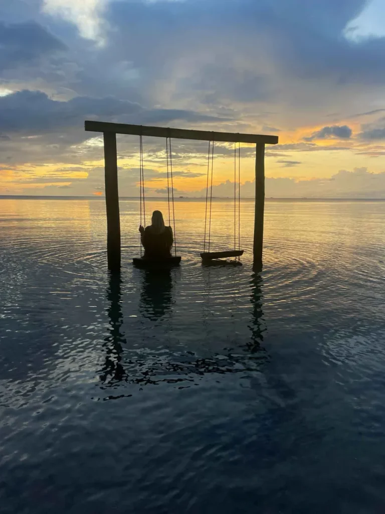 silhoutte from wooden frame with two swings and one person sitting on a swing in the sea at sunset sunrise at Mariposa Beach Resort in placencia belize
