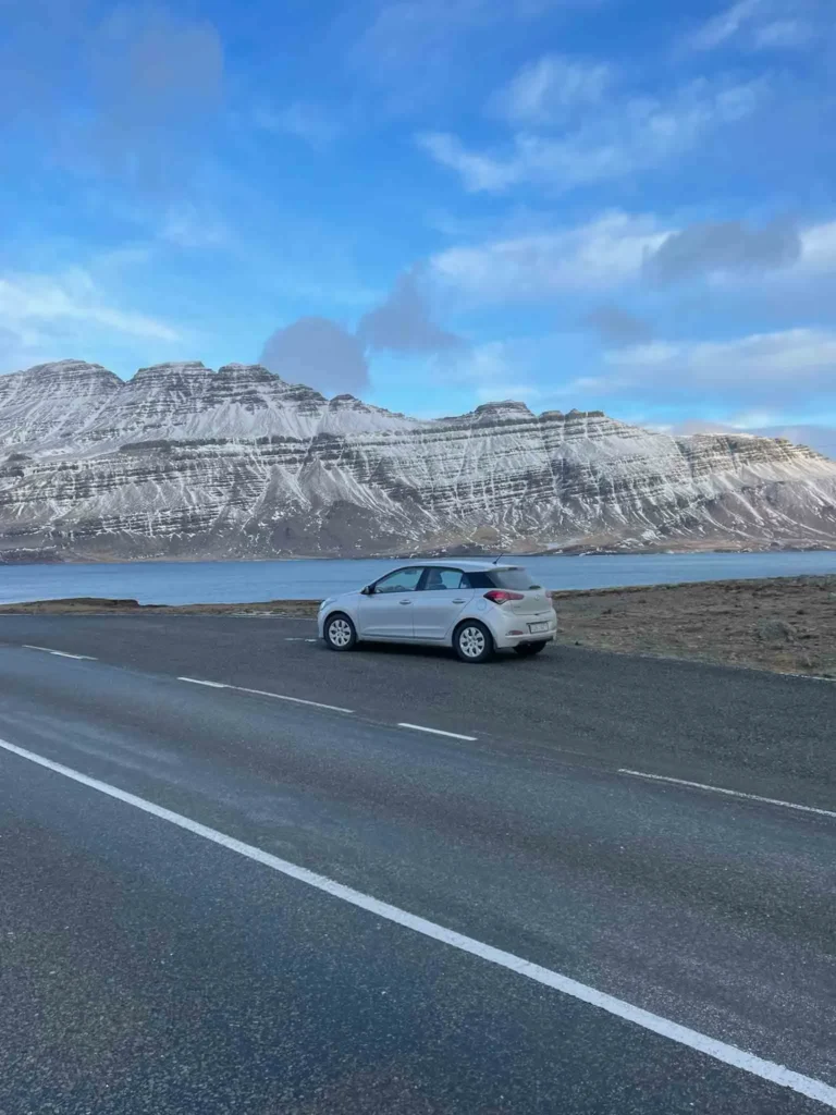 Rental car for my trip around Iceland in winter car parking on the side of the road with partially snowy mountains and the sea in the back in iceland