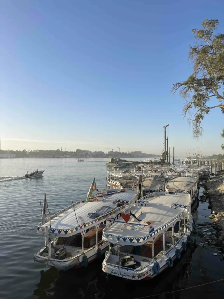 multiple boats docking next to each other on the side of a river with blue skies