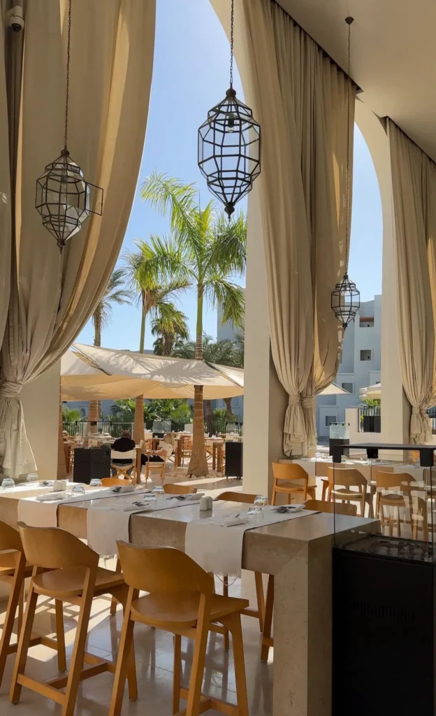 stylish hotel restaurant with huge white curtains, palmtrees, chairs and tables