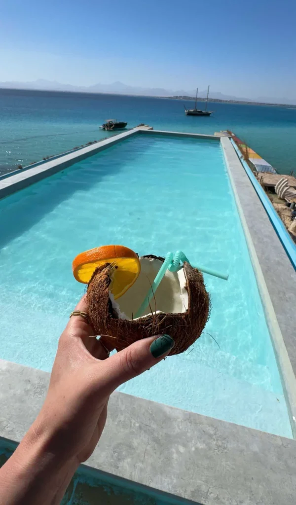 hand holding a coconut drink with a large infinity pool in the background overlooking the ocean