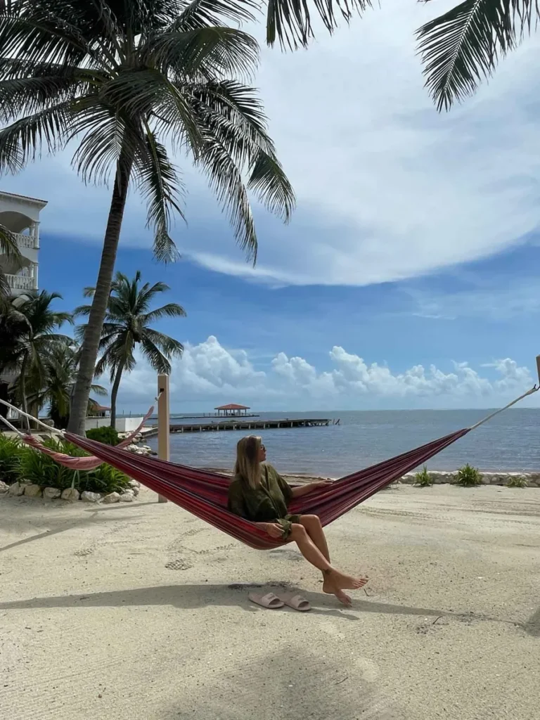 woman sitting in a hammoch between two palm trees at the beach with more palm trees and a view at the sea in san pedro ambergris caye belize