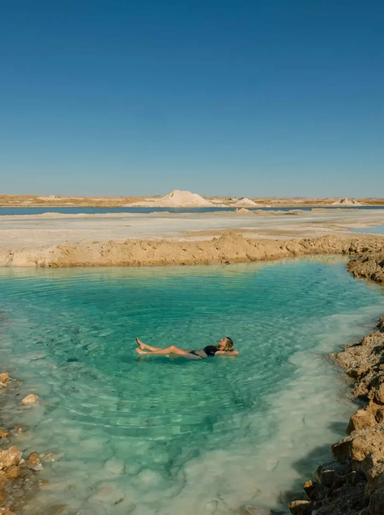 woman floating in a salt lake in a desert-like landscape with blue skies