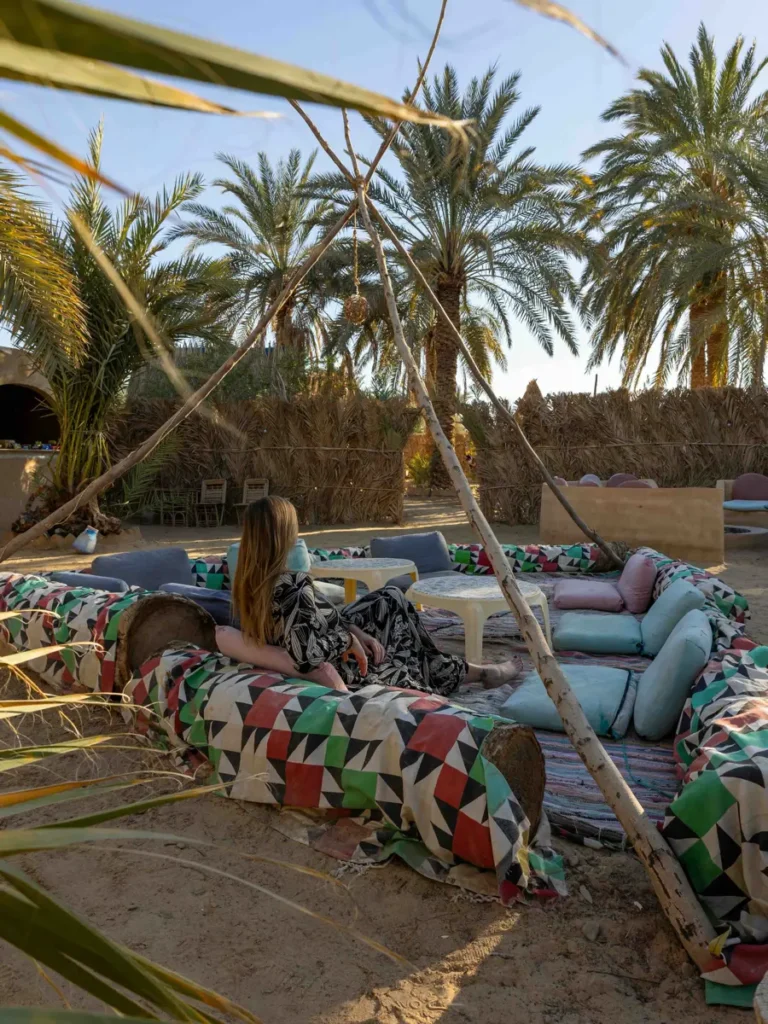 a woman relaxing at a lounge full of colourful carpets below palmtrees