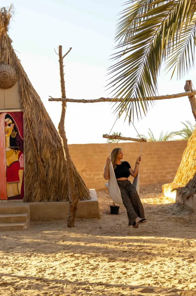 woman sitting on a hammock swing in the desert below a palmtree 