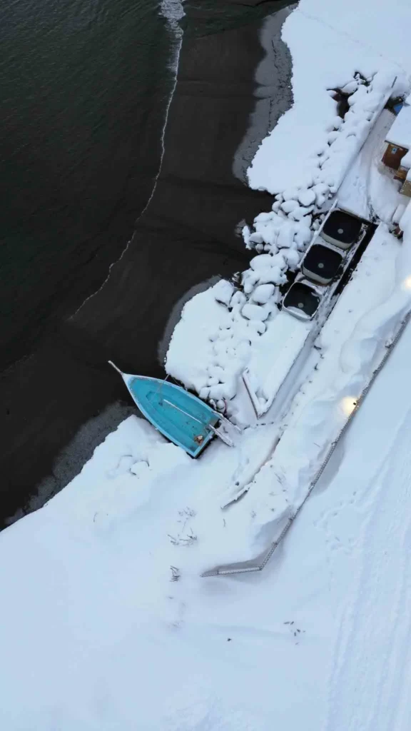 Hauganes Hot tubs from above drone shot of a beach area with a boat as a hot tub and three additional hot tubs in a snowy landscape at huaganes hot tubs in iceland