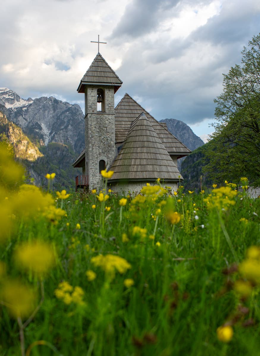 image church in Theth Albania taken during dawn with yellow flowers in the foreground - Albania travel guide