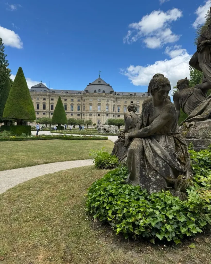 Gardens with statues, grass, flowers and trees with a beautiful castle-like building in Würzburg, Germany