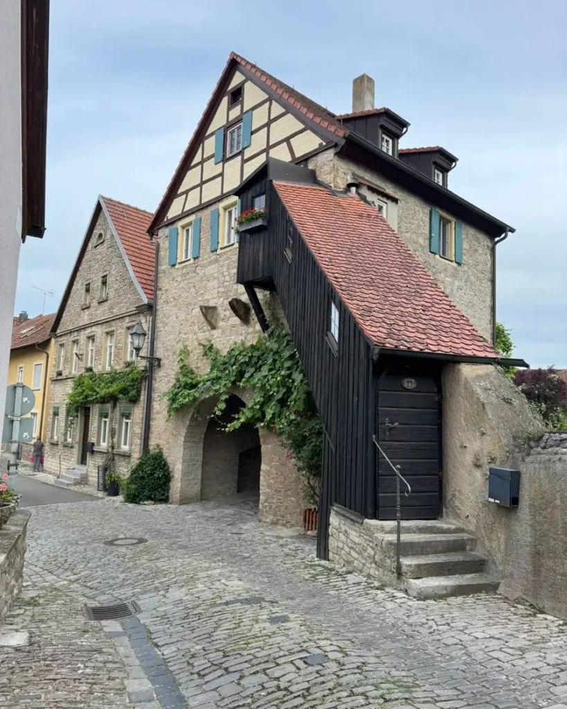 Historic town gate with a half-timbered house built on top with a staircase leading and cobblestone roads in front in Dettelbach