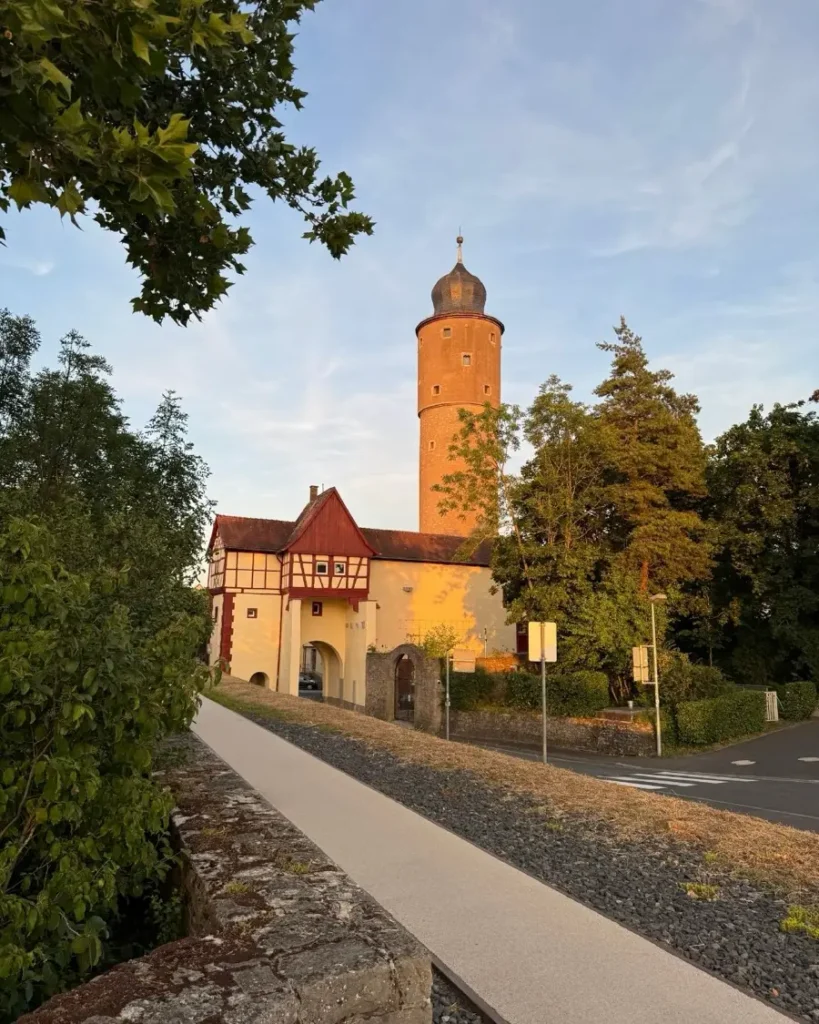 Golden light shining on a historic gate with a house and watch tower surrounded by trees and a walkway in Ochsenfurt, Germany