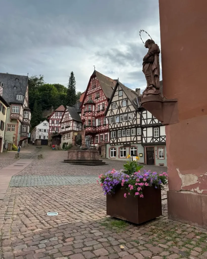 Half-timbered houses on a medieval square with a fountain, some flowers, cobblestone roads and a statue in Miltenberg - one of the most beautiful towns in Germany