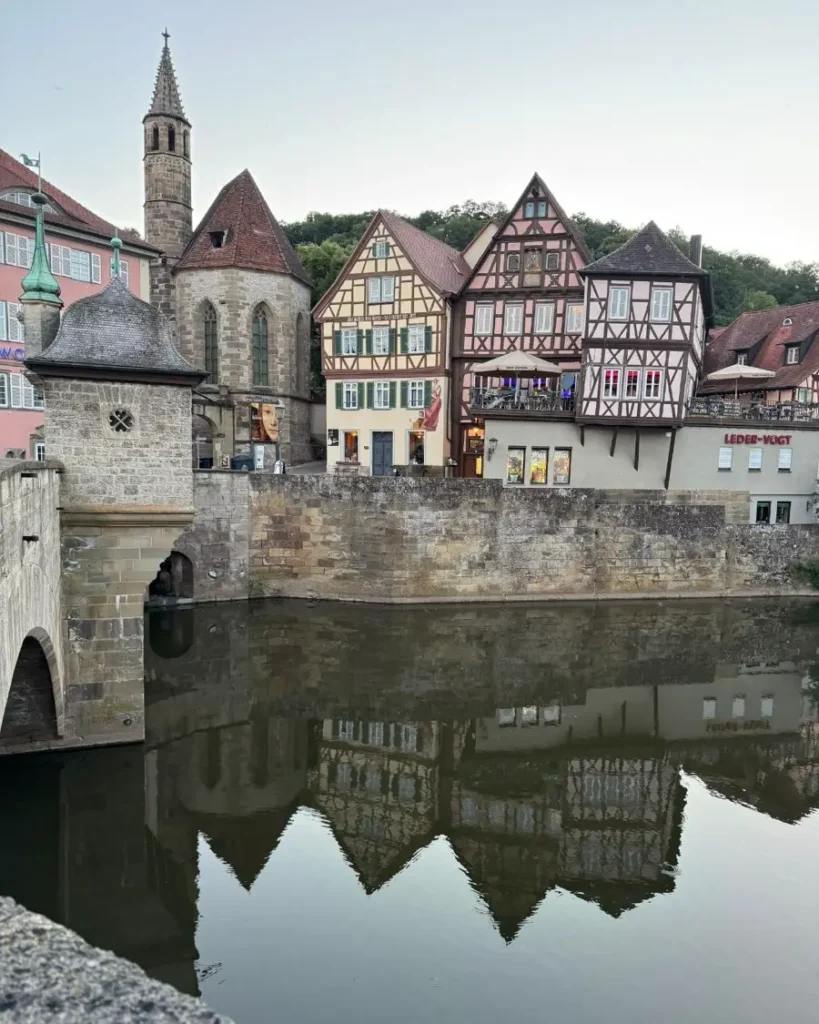 Half-timbered houses and a church along a river with perfect reflection in the water and a historic bridge with arches in Schwäbisch Hall