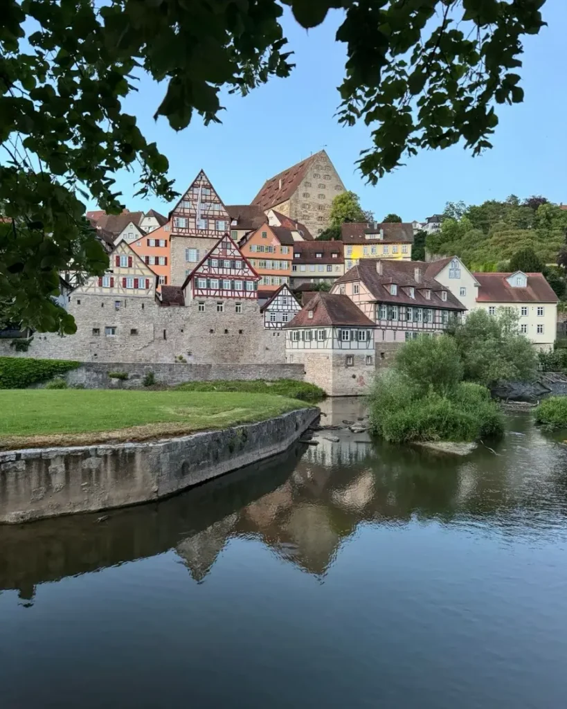 Half-timbered houses built on a hill of an old town along a river with a man-made island and dam in Schwäbisch Hall, Germany