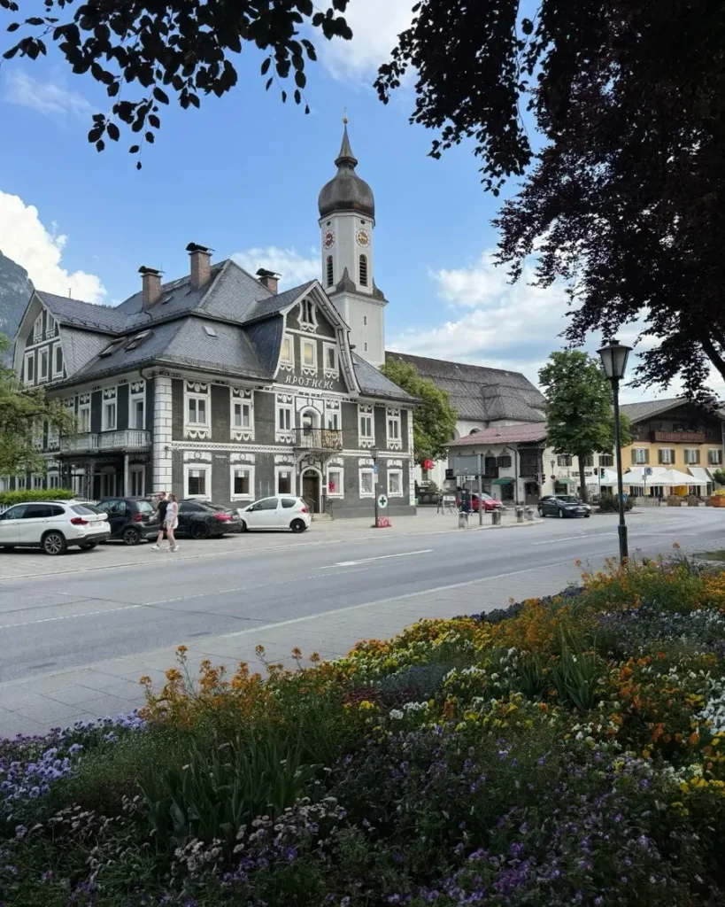 Historic mountain town with a traditional church and colourful houses, flowers and trees on the other side of the road in Garmisch-Partenkirchen