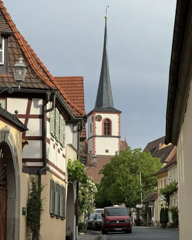 A road in a charing town leading to a church lined with some parked cars and traditional houses in Sommerach, Germany