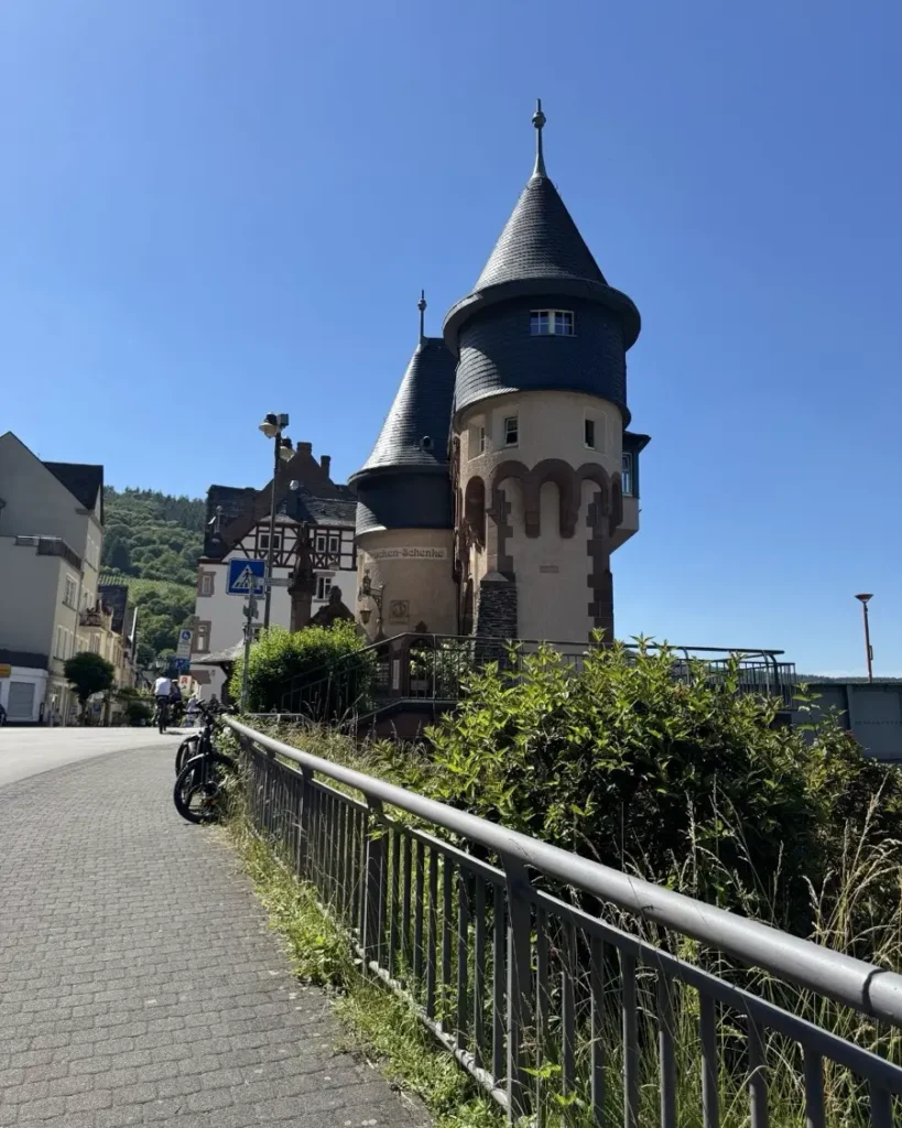 A walkway with handles on the side of the road leading to historic bridge towers and a small old town in Traben-Trarbach