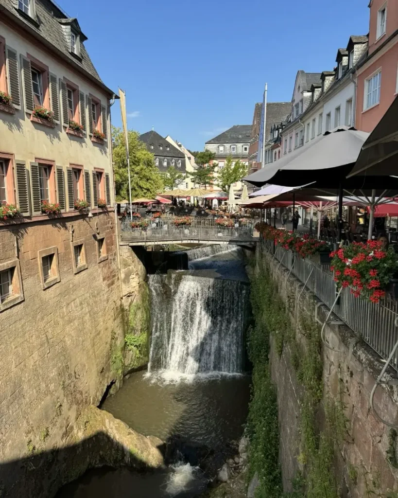 Man-made waterfall in the historic town of Saarburg with a bridge leading over it, houses and restaurant outdoor seating areas