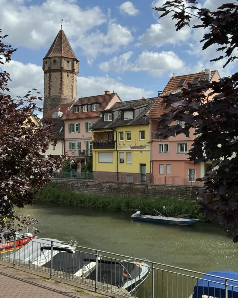 Colourful housefront with a medieval tower along a small river with a couple of boats docked alongside the shores in Wertheim am Main, Germany