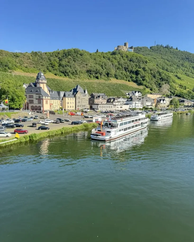 A riverside town along the Moselle with green hills, historic houses and buildings, docked ship and hillside castle - Bernkastel-Kües, Germany