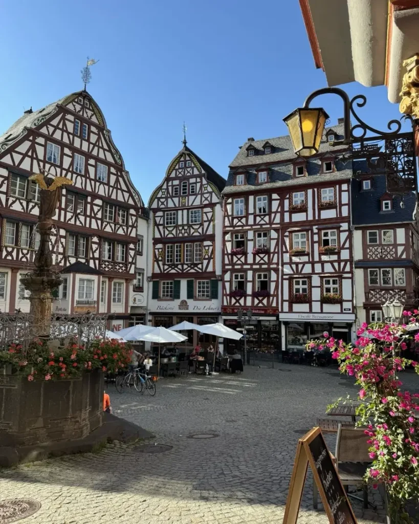 A charming old town square with a fountain, typical half-timbered houses, outdoor seating area and flowers in Bernkastel-Küs