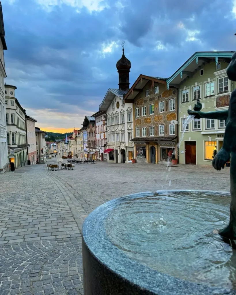 A fountain on a cobblestone road of the historic old town with colourful houses and a church in Bad Tölz, Germany