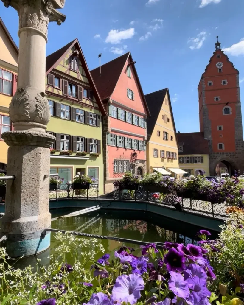 A fountain surrounded by flowers in a colourful fairytale town in Germany called Dinkelsbühl