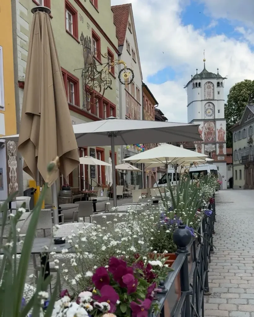 Old town with a historic tower, flowers, a cafe with outdoor seating area and traditional houses in Wangen, Germany