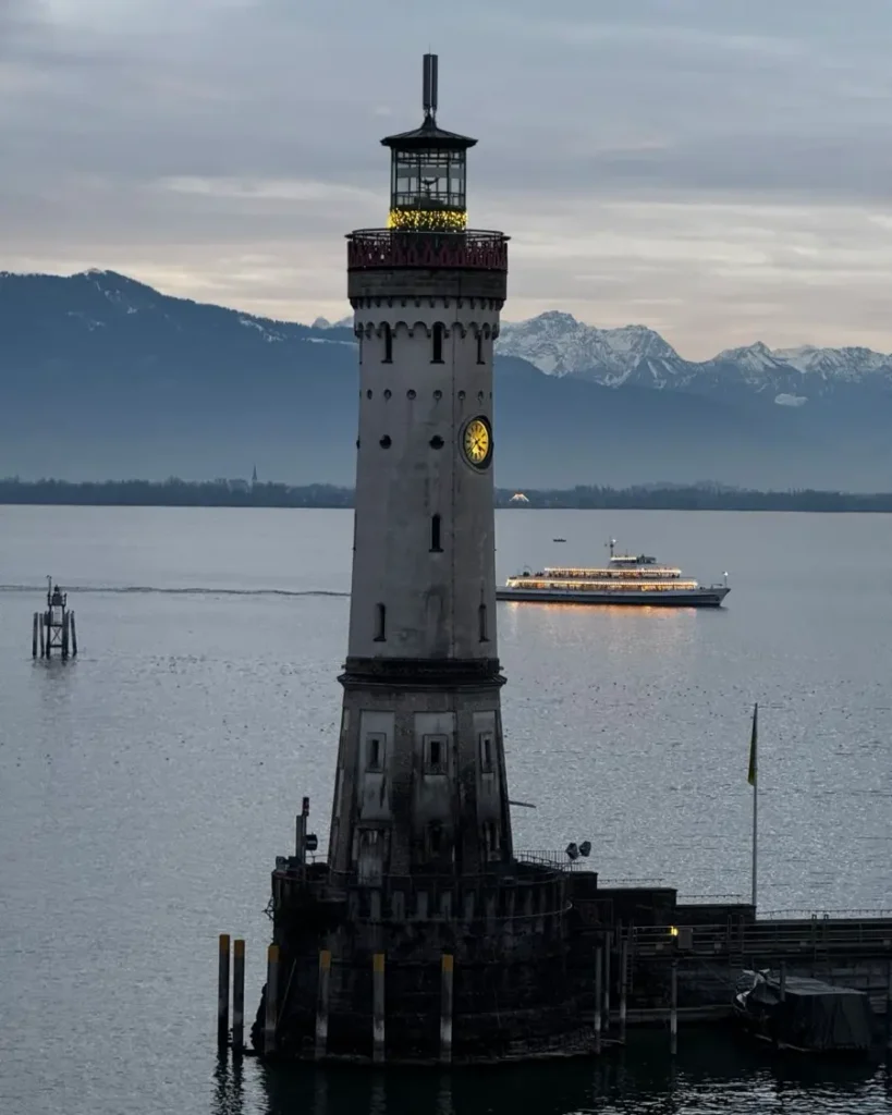 Lighthouse at Lake Constance with a ship passing and mountains in the distance in Lindau am Bodensee, Germany